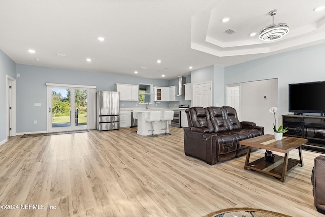 living room with sink, light hardwood / wood-style flooring, and a raised ceiling