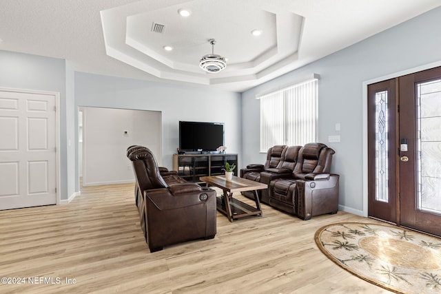 living room with a textured ceiling, light wood-type flooring, and a raised ceiling