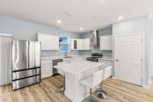 kitchen with appliances with stainless steel finishes, wall chimney exhaust hood, a center island, and light hardwood / wood-style flooring