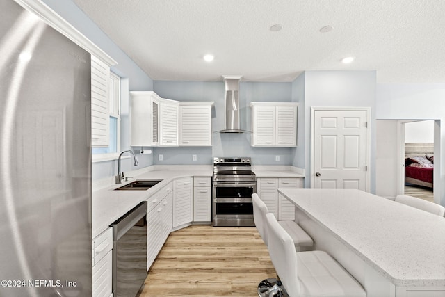 kitchen with wall chimney exhaust hood, a breakfast bar area, light hardwood / wood-style flooring, sink, and appliances with stainless steel finishes