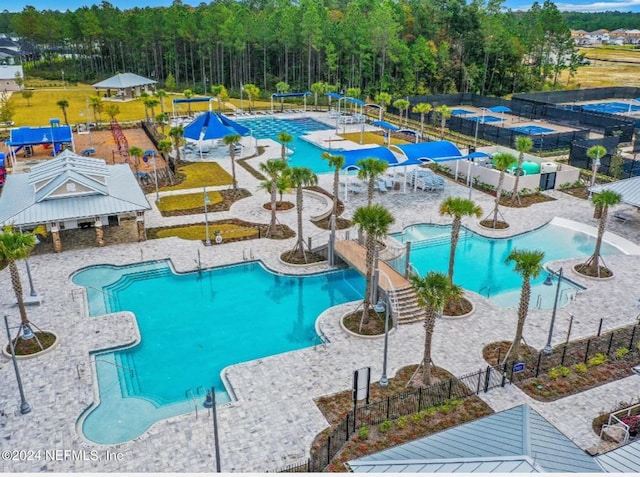 community pool with a water play area, a patio area, a water slide, and fence