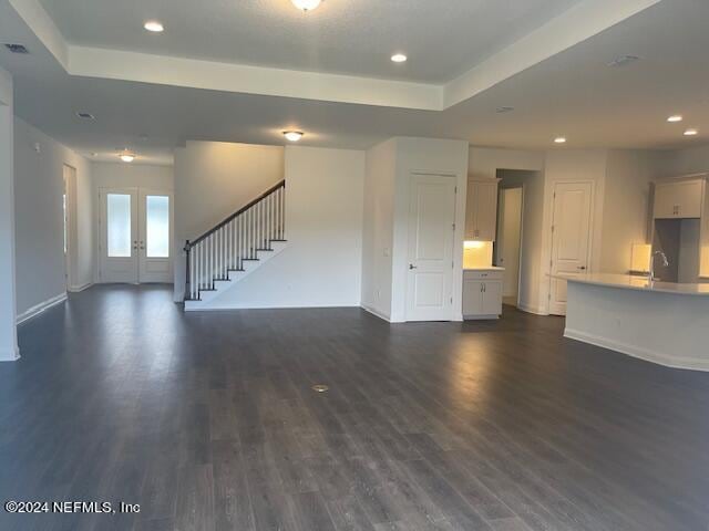 unfurnished living room featuring dark wood-type flooring, french doors, and a tray ceiling