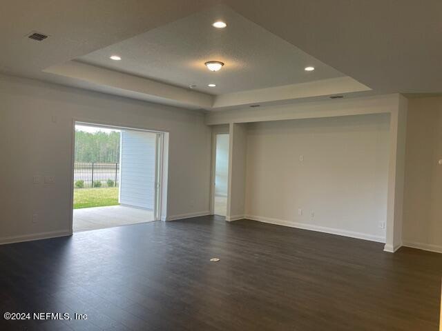 empty room with a tray ceiling and dark hardwood / wood-style flooring