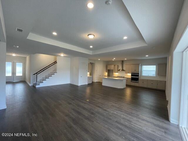 unfurnished living room with dark wood-type flooring, a tray ceiling, and french doors