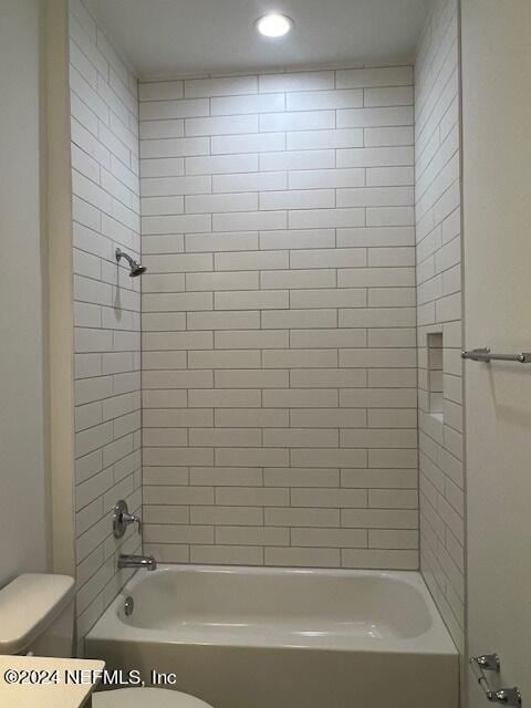 bathroom featuring toilet and tiled shower / bath