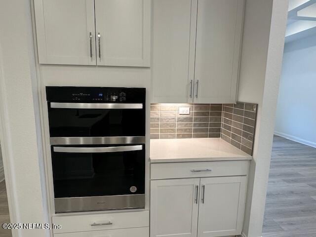 kitchen featuring white cabinetry, light hardwood / wood-style floors, double oven, and decorative backsplash