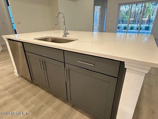 kitchen with dishwasher, an island with sink, sink, light stone countertops, and light wood-type flooring