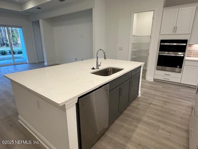 kitchen featuring sink, dishwasher, white cabinetry, a center island with sink, and light wood-type flooring