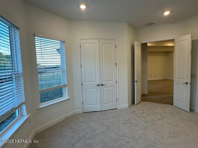 unfurnished bedroom featuring multiple windows, light carpet, and a closet