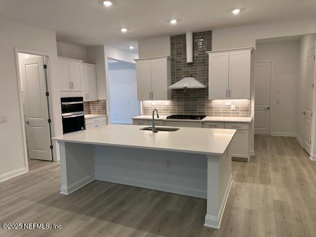 kitchen featuring white cabinetry, sink, stainless steel gas cooktop, light hardwood / wood-style floors, and a center island with sink