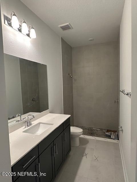 bathroom featuring vanity, toilet, a textured ceiling, and tiled shower