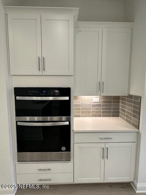 kitchen with double oven, backsplash, white cabinets, and hardwood / wood-style flooring