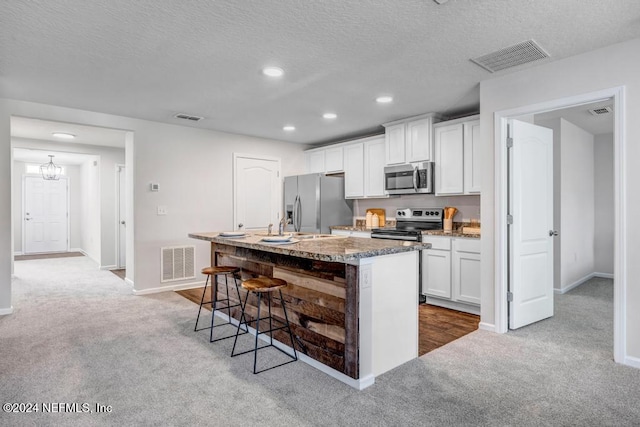 kitchen with white cabinetry, light carpet, stainless steel appliances, and a center island with sink