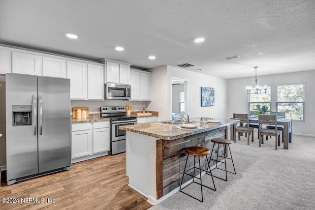 kitchen with white cabinetry, appliances with stainless steel finishes, pendant lighting, and a center island with sink