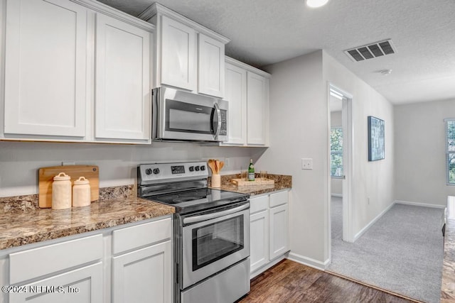 kitchen with light stone countertops, appliances with stainless steel finishes, white cabinetry, and dark hardwood / wood-style flooring