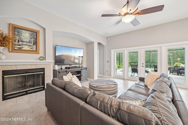 living room with a fireplace, french doors, a textured ceiling, ceiling fan, and light tile patterned floors