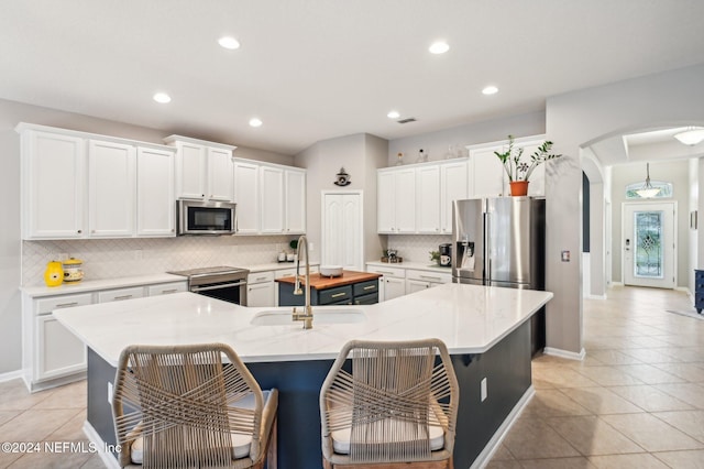 kitchen with sink, appliances with stainless steel finishes, white cabinetry, and an island with sink