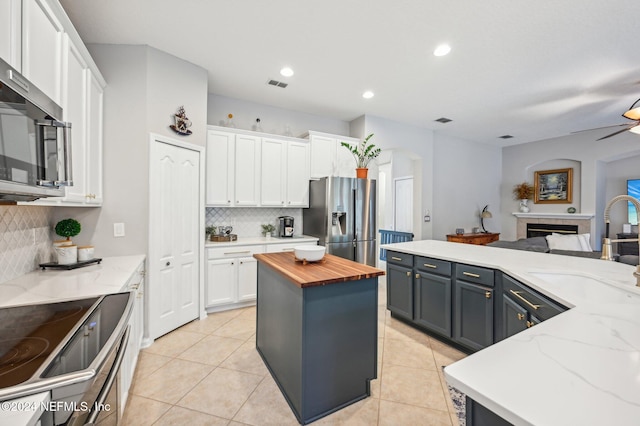 kitchen featuring a kitchen island, stainless steel appliances, white cabinets, butcher block countertops, and a fireplace