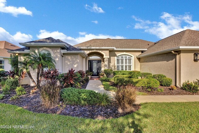mediterranean / spanish-style house with a shingled roof, stucco siding, and a front lawn