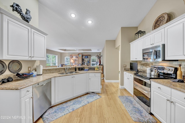 kitchen with kitchen peninsula, sink, white cabinets, light wood-type flooring, and appliances with stainless steel finishes