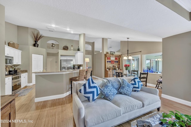 living room with high vaulted ceiling, a textured ceiling, an inviting chandelier, and light wood-type flooring