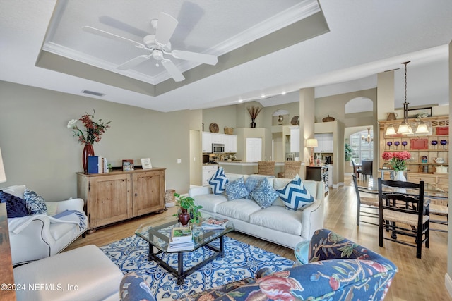 living room with crown molding, ceiling fan, a raised ceiling, and light wood-type flooring