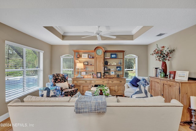 living room featuring light hardwood / wood-style flooring, ceiling fan, crown molding, and a raised ceiling