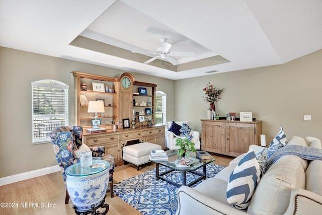 living room with a tray ceiling, light wood-type flooring, and ceiling fan