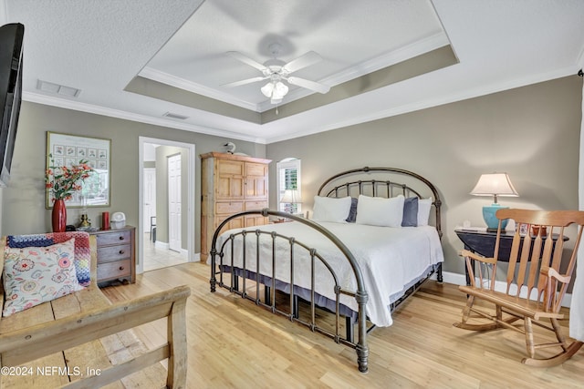 bedroom with light hardwood / wood-style flooring, ornamental molding, a raised ceiling, and ceiling fan