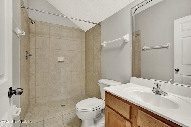 bathroom with a textured ceiling, toilet, tiled shower, vanity, and tile patterned flooring