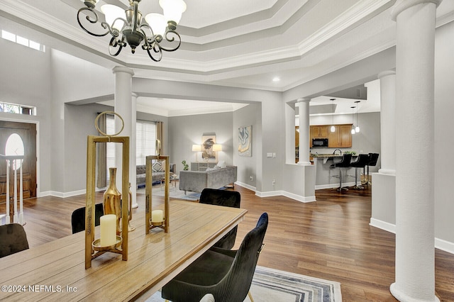 dining area with hardwood / wood-style flooring, a tray ceiling, ornamental molding, ornate columns, and a notable chandelier