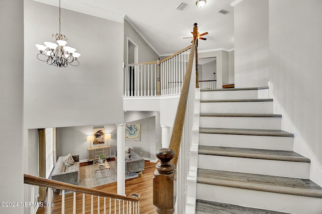 staircase with a towering ceiling, wood-type flooring, ornamental molding, and ceiling fan with notable chandelier