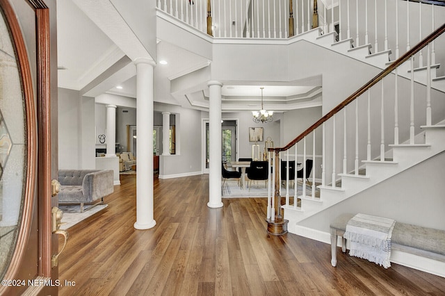 foyer entrance featuring a towering ceiling, crown molding, hardwood / wood-style floors, and decorative columns