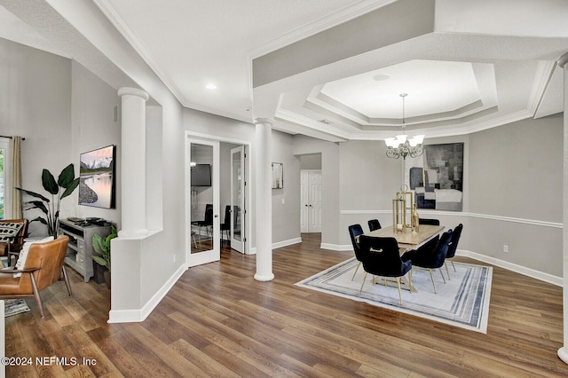 dining space featuring wood-type flooring, a tray ceiling, decorative columns, crown molding, and a chandelier