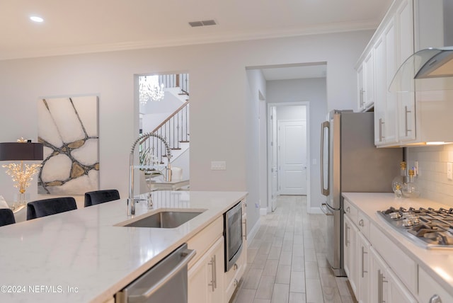 kitchen with wall chimney range hood, a breakfast bar area, sink, white cabinetry, and appliances with stainless steel finishes