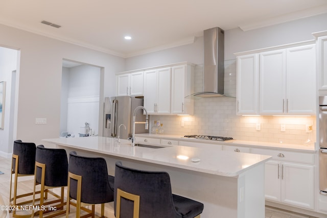 kitchen with appliances with stainless steel finishes, an island with sink, wall chimney range hood, and white cabinets