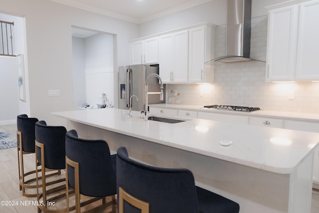 kitchen with appliances with stainless steel finishes, white cabinetry, a kitchen island with sink, wall chimney exhaust hood, and sink