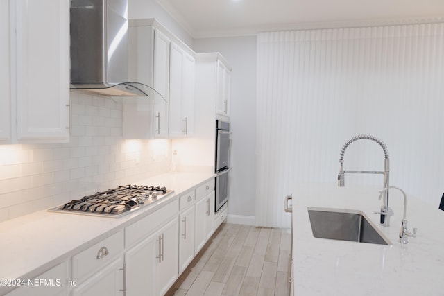 kitchen featuring wall chimney range hood, backsplash, sink, white cabinets, and appliances with stainless steel finishes