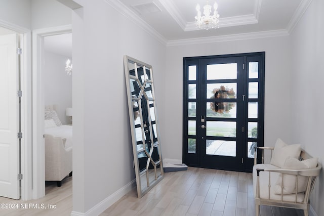 foyer with a raised ceiling, ornamental molding, an inviting chandelier, and light wood-type flooring