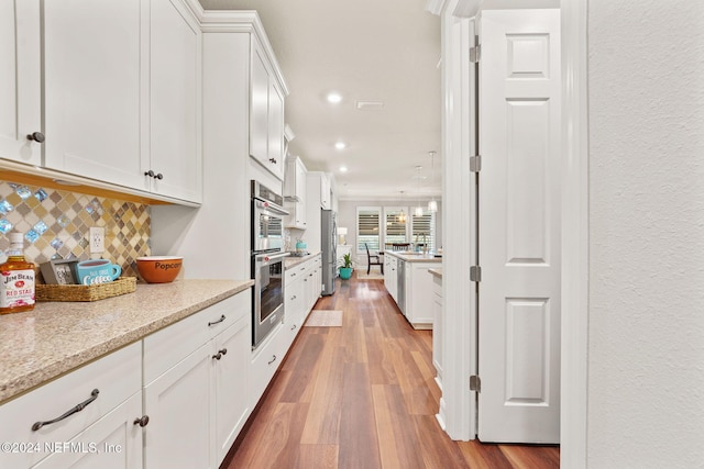 kitchen with wood finished floors, white cabinetry, stainless steel appliances, and decorative backsplash