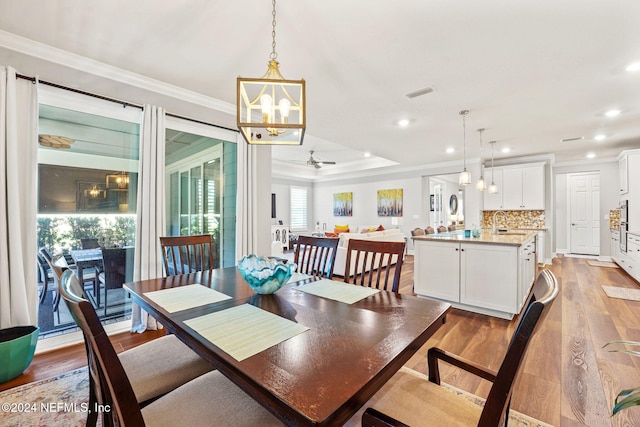 dining room featuring light wood-type flooring, ornamental molding, ceiling fan with notable chandelier, and recessed lighting