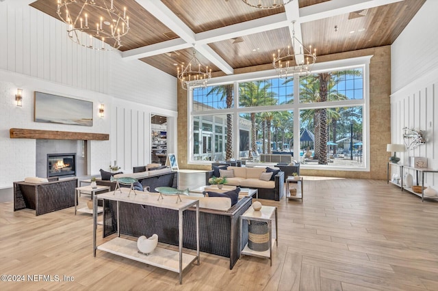 living area with a towering ceiling, a glass covered fireplace, a chandelier, and wood ceiling
