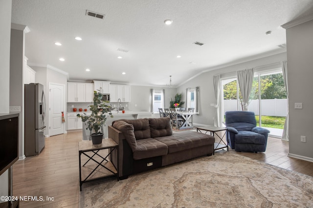 living room with light hardwood / wood-style floors, lofted ceiling, a textured ceiling, and crown molding