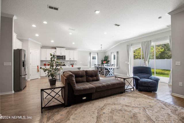 living room with a textured ceiling, vaulted ceiling, light hardwood / wood-style flooring, crown molding, and sink