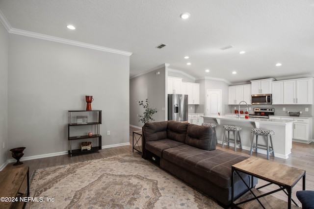 living room with ornamental molding, sink, light wood-type flooring, and vaulted ceiling