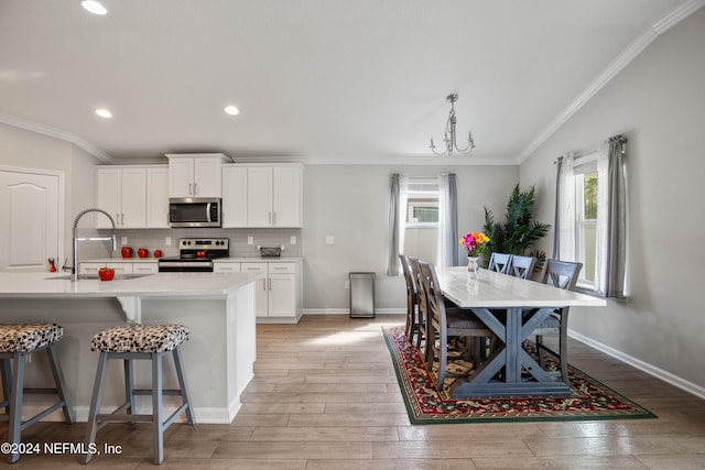 kitchen featuring a center island with sink, sink, white cabinetry, appliances with stainless steel finishes, and light hardwood / wood-style floors