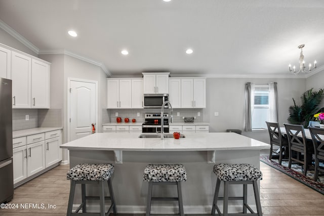 kitchen featuring appliances with stainless steel finishes, white cabinetry, a center island with sink, and light hardwood / wood-style floors