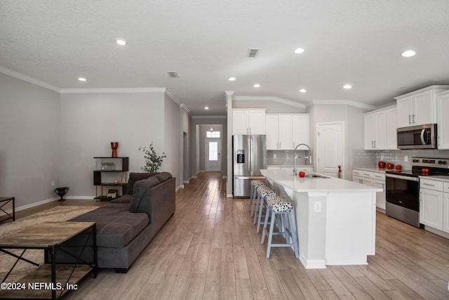 kitchen with a center island with sink, appliances with stainless steel finishes, a kitchen bar, light wood-type flooring, and sink