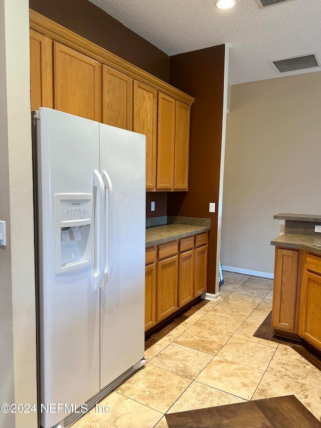 kitchen with light tile patterned floors, a textured ceiling, and white refrigerator with ice dispenser