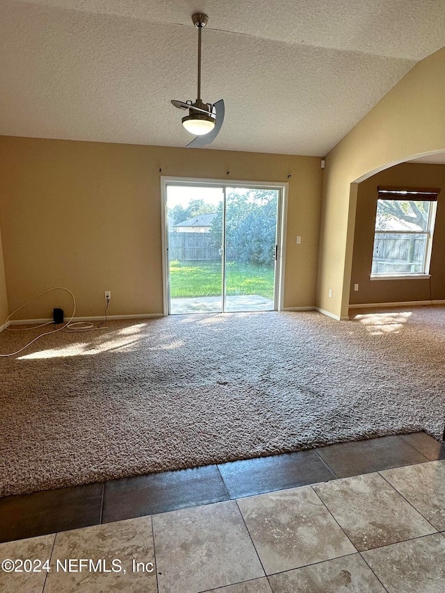 spare room featuring tile patterned floors, vaulted ceiling, a textured ceiling, and a healthy amount of sunlight